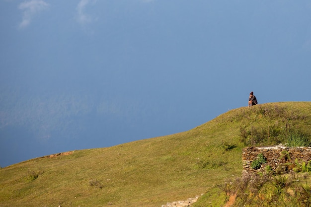 Un homme est assis sur une colline devant un ciel bleu.