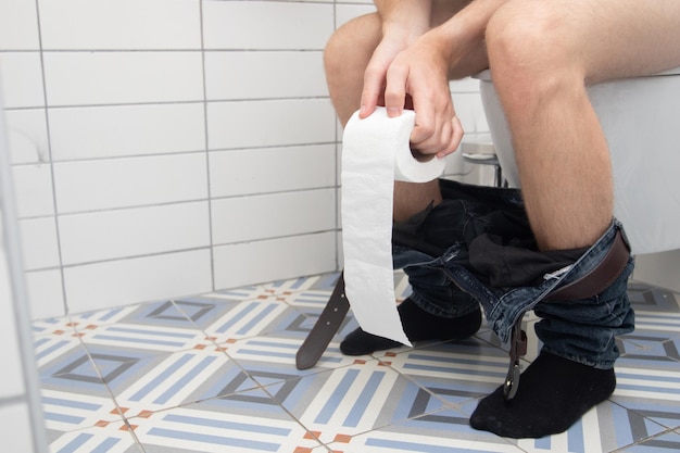 Photo l'homme est assis sur la cuvette des toilettes et tient du papier toilette