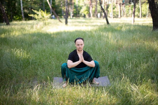 L'homme est assis dans un asana pratiquant le yoga dans le parc sur l'herbe verte. Journée internationale du yoga