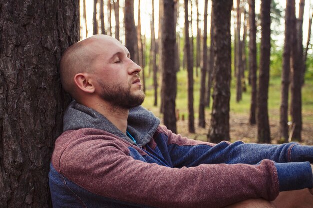 L'homme est assis dans les bois avec le dos sur un arbre