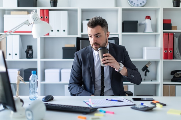 Un Homme Est Assis Dans Le Bureau à La Table, Boit Du Café Et Regarde L'écran De L'ordinateur.