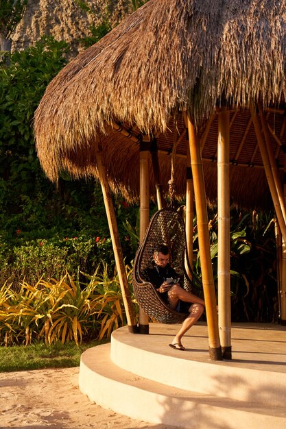 Un homme est assis dans un œuf de berceau dans une pergola de paille en profitant du coucher de soleil