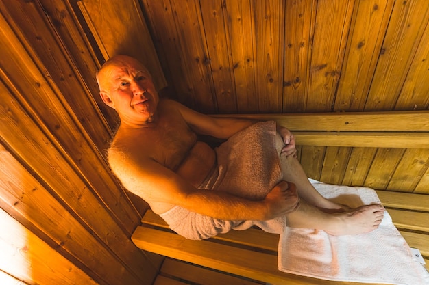 Un homme est assis dans un sauna avec une serviette sur sa jambe.