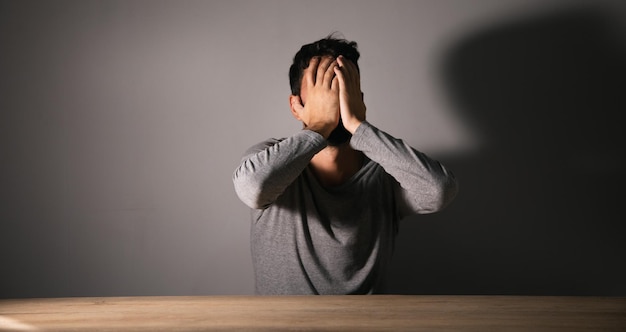 Un homme est assis devant une table couvrant son visage avec ses mains