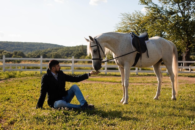 L'homme est assis sur l'herbe et nourrit un cheval