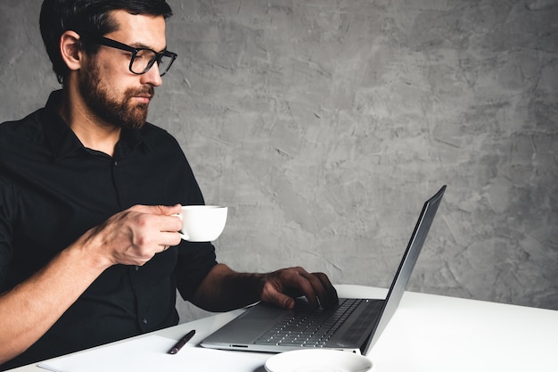 Un homme est assis avec un ordinateur portable dans une chemise noire. Concept d'entreprise, travail. Routine de bureau. Efforts de propriété