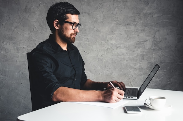Un homme est assis avec un ordinateur portable dans une chemise noire.
