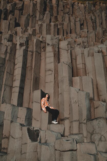 un homme est assis sur un rocher devant une grande colonne de granit