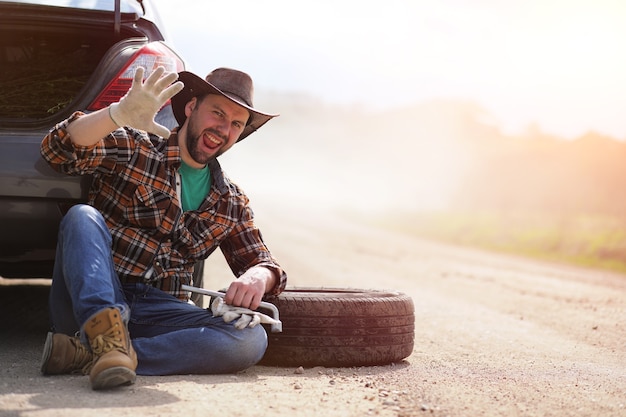 L'homme est assis sur la route près de la voiture dans la nature