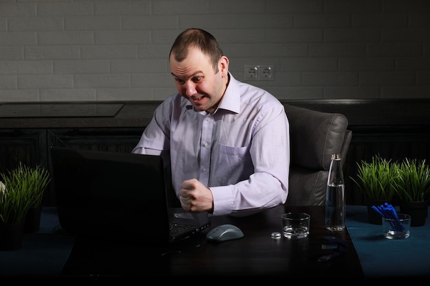 L'homme est assis à son bureau et travaille sur un ordinateur portable