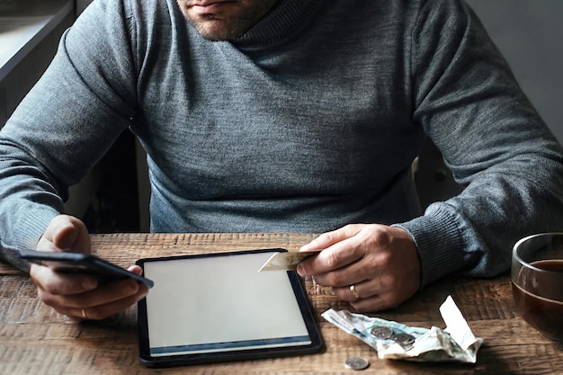 un homme est assis à une table devant lui avec une tablette et une carte bancaire il effectue un paiement en ligne