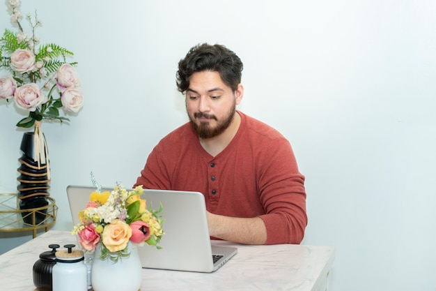 Un homme est assis à une table avec un ordinateur portable et un bouquet de fleurs dessus