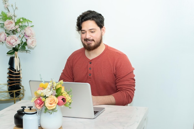 Un homme est assis à une table avec un ordinateur portable et des fleurs dessus