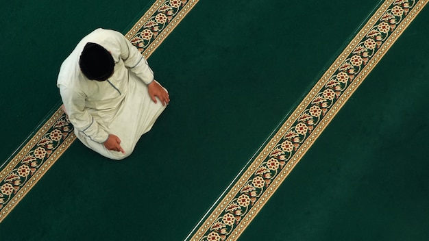 Un homme est assis sur un tapis de prière dans une mosquée.