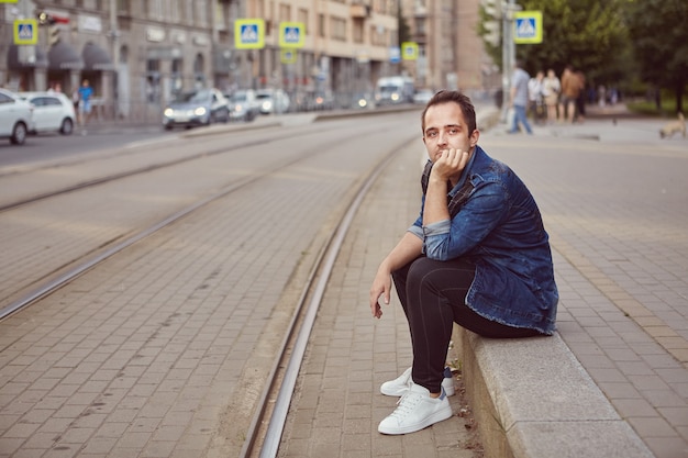 L'homme est assis sur le trottoir près de la voie ferrée.