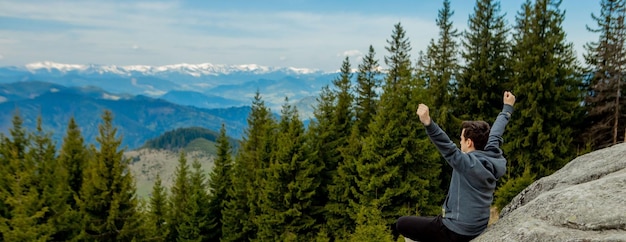 Un homme est haut dans les montagnes contre le ciel célébrant la victoire en levant les mains