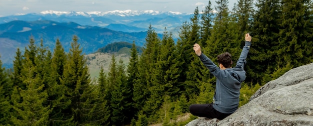 Un homme est haut dans les montagnes contre le ciel, célébrant la victoire, levant les mains.