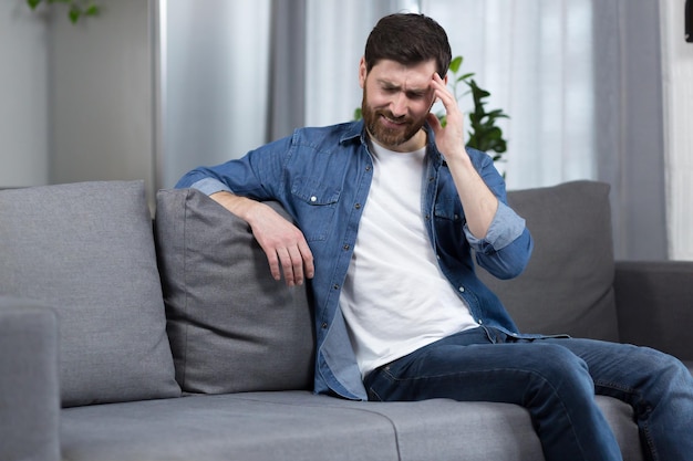 L'homme est à la maison le patient est assis sur le canapé a un mal de tête sévère