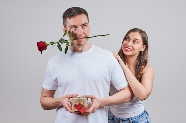 Un homme est sceptique quant à des vacances, un cadeau, tandis qu'une femme souriante amoureuse le regarde en le serrant par les épaules.