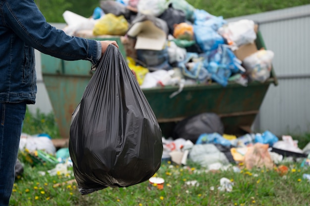 L'homme Est Titulaire D'un Sac En Plastique Poubelle Plein En Face De Poubelle Débordant à L'extérieur à La Campagne