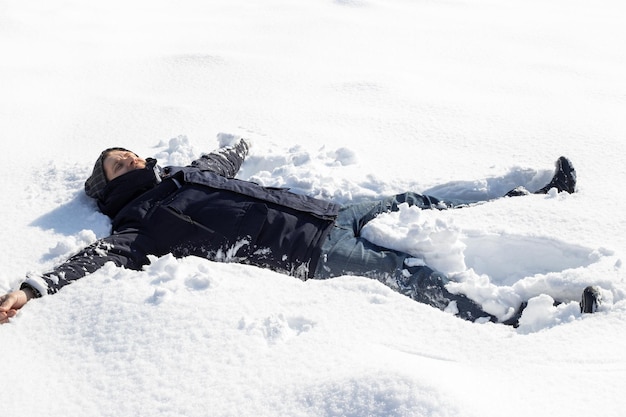 Un homme est tombé dans une congère avec ses bras tendus à ses côtés Plaisirs d'hiver à l'extérieur par une journée ensoleillée