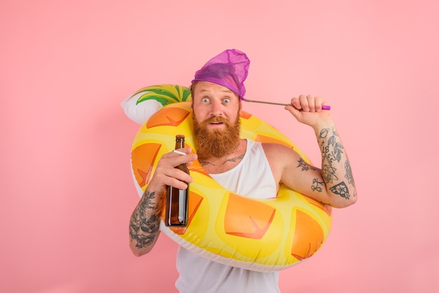 L'homme étonné est prêt à nager avec une bouée de sauvetage de beignet avec de la bière et une cigarette à disposition