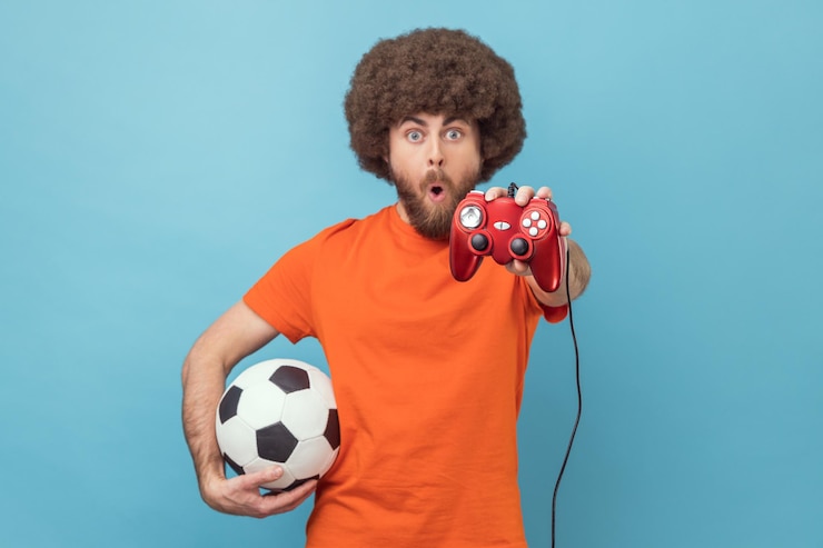 Photo homme étonné tenant un ballon de football et montrant un joypad rouge au jeu vidéo de la caméra