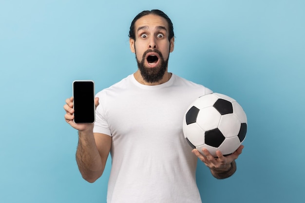 Un homme étonné tenant un ballon de football et un smartphone vide affiche un billet noir pour le championnat