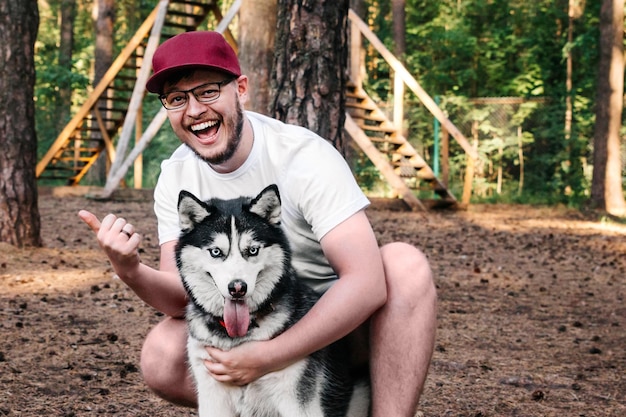 L'homme étreint le chien rit et montre son pouce Le Husky montre sa langue