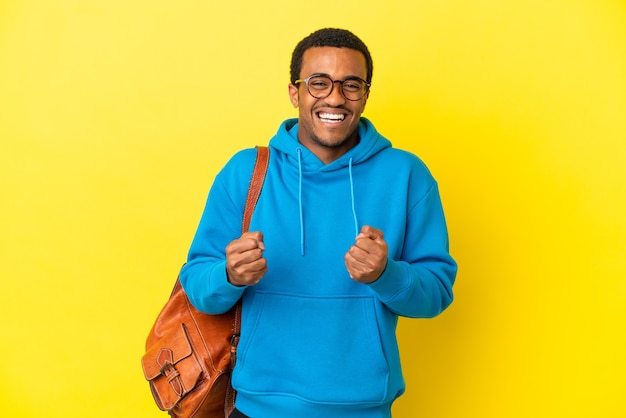 Homme étudiant afro-américain sur fond jaune isolé célébrant une victoire en position de vainqueur