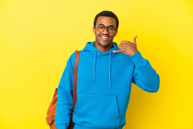 Homme étudiant afro-américain sur fond jaune isolé faisant un geste de téléphone. Rappelle-moi signe
