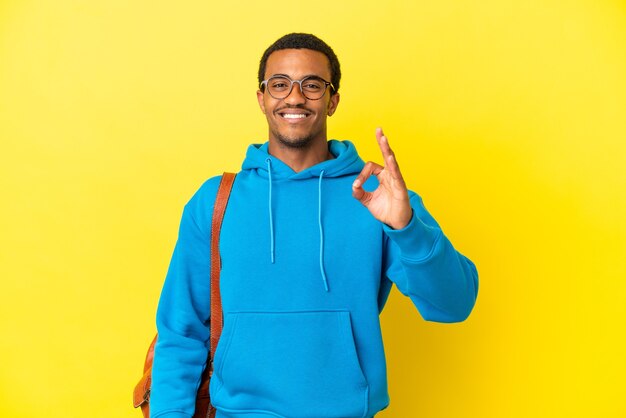 Homme étudiant afro-américain sur fond jaune isolé montrant un signe ok avec les doigts