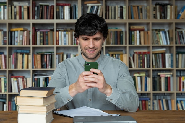Homme étudiant à l'aide de l'apprentissage de smartphone assis à des livres dans la bibliothèque universitaire