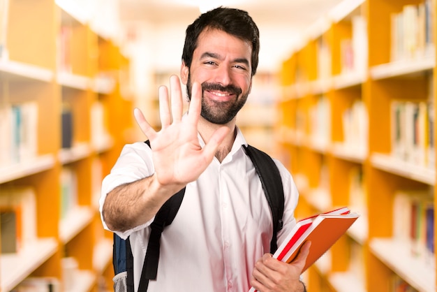 Homme étudiant comptant cinq sur une bibliothèque défocalisée