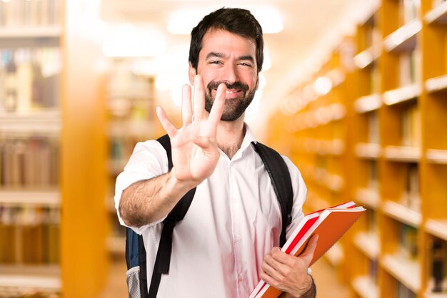 Homme étudiant comptant quatre sur une bibliothèque défocalisée