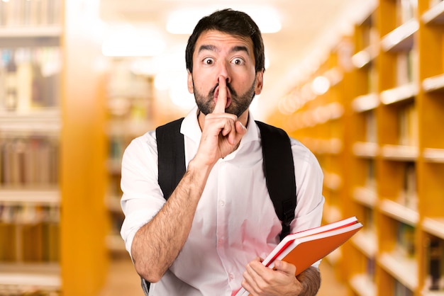 Homme étudiant faisant un geste de silence sur une bibliothèque défocalisée