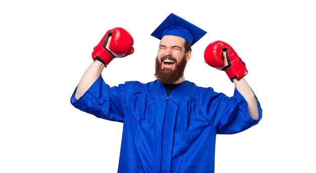 Homme étudiant gai célébrant avec diplôme avec des gants de boxe