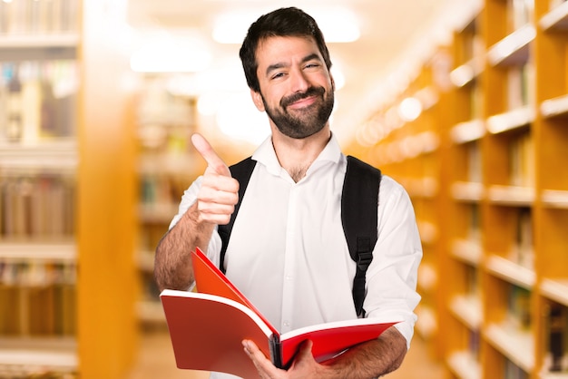 Homme étudiant avec le pouce sur la bibliothèque défocalisée