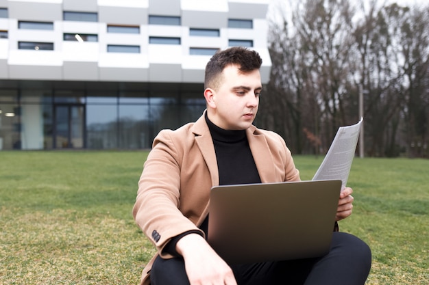 L'homme étudie assis avec un cahier dans ses mains sur l'herbe près de l'université