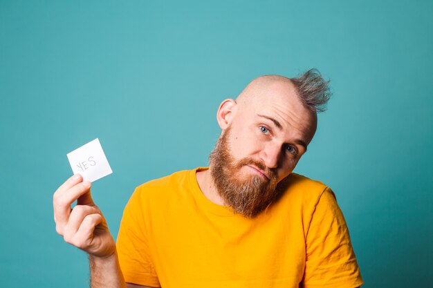 Homme Européen Barbu En Chemise Jaune Isolé, Tenant Oui Avec Surprise Et Expression émerveillée Visage Excité.