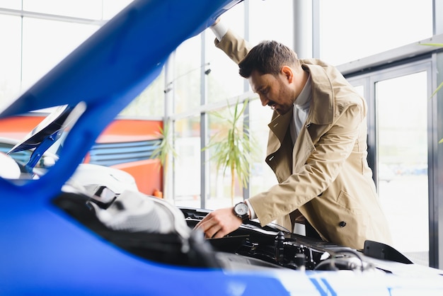 Homme examinant le moteur d'une nouvelle automobile chez le concessionnaire automobile à la recherche sous le capot