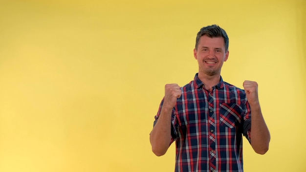 Homme excité en chemise à carreaux levant les poings en signe d'acclamation sur fond jaune, il soutient et encourage...