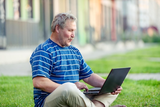Un homme excité est surpris par le contenu en regardant un ordinateur portable sur la pelouse de la ville Le concept de la vie moderne dans la ville