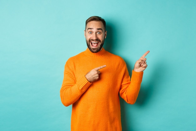 Homme excité faisant une annonce, pointant du doigt à droite votre logo, debout