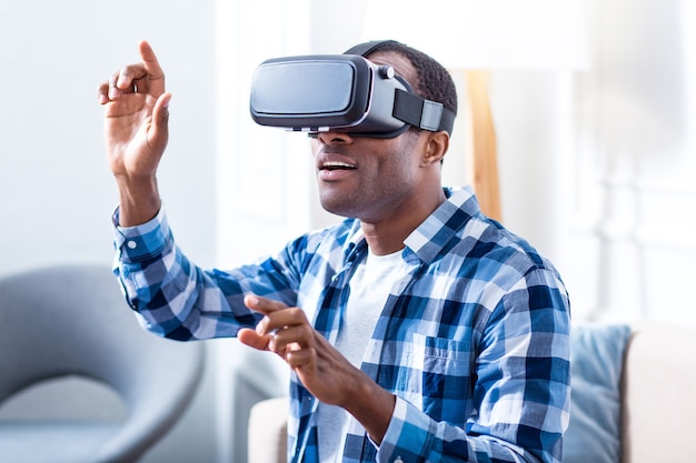 Homme excité joyeux positif portant des lunettes de réalité virtuelle et souriant tout en testant de nouvelles technologies