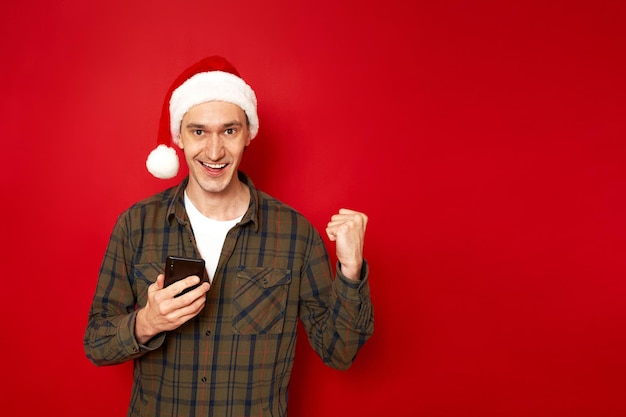 un homme excité avec un téléphone à la main célèbre la victoire dans un jeu d'application mobile isolé sur fond rouge