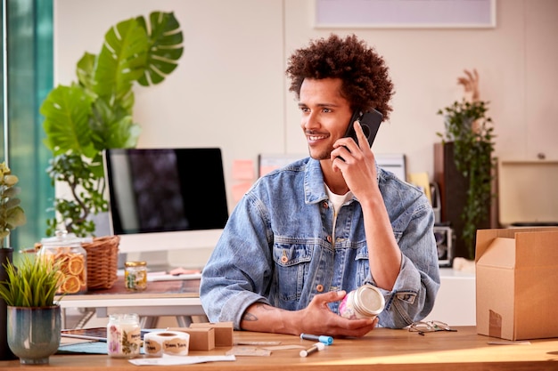 Homme exécutant des affaires en ligne faisant des bougies de boutique à la maison parlant sur le téléphone portable