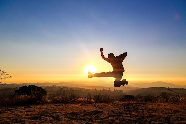 Homme exécutant un coup de pied volant sur une surface floue qui ressemble à une montagne au coucher du soleil