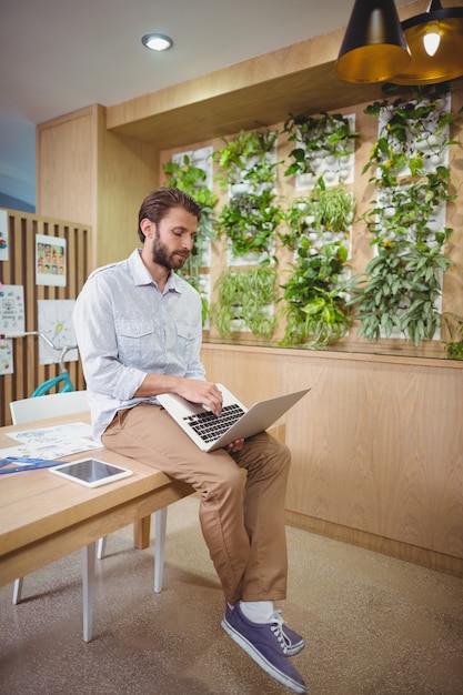 Homme exécutif assis sur un bureau et utilisant un ordinateur portable