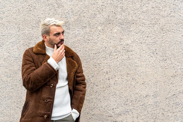 Homme avec expression de méditation avec la main au menton, debout contre un fond de mur, regardant sur le côté pour imaginer quelque chose, expression faciale de réflexion